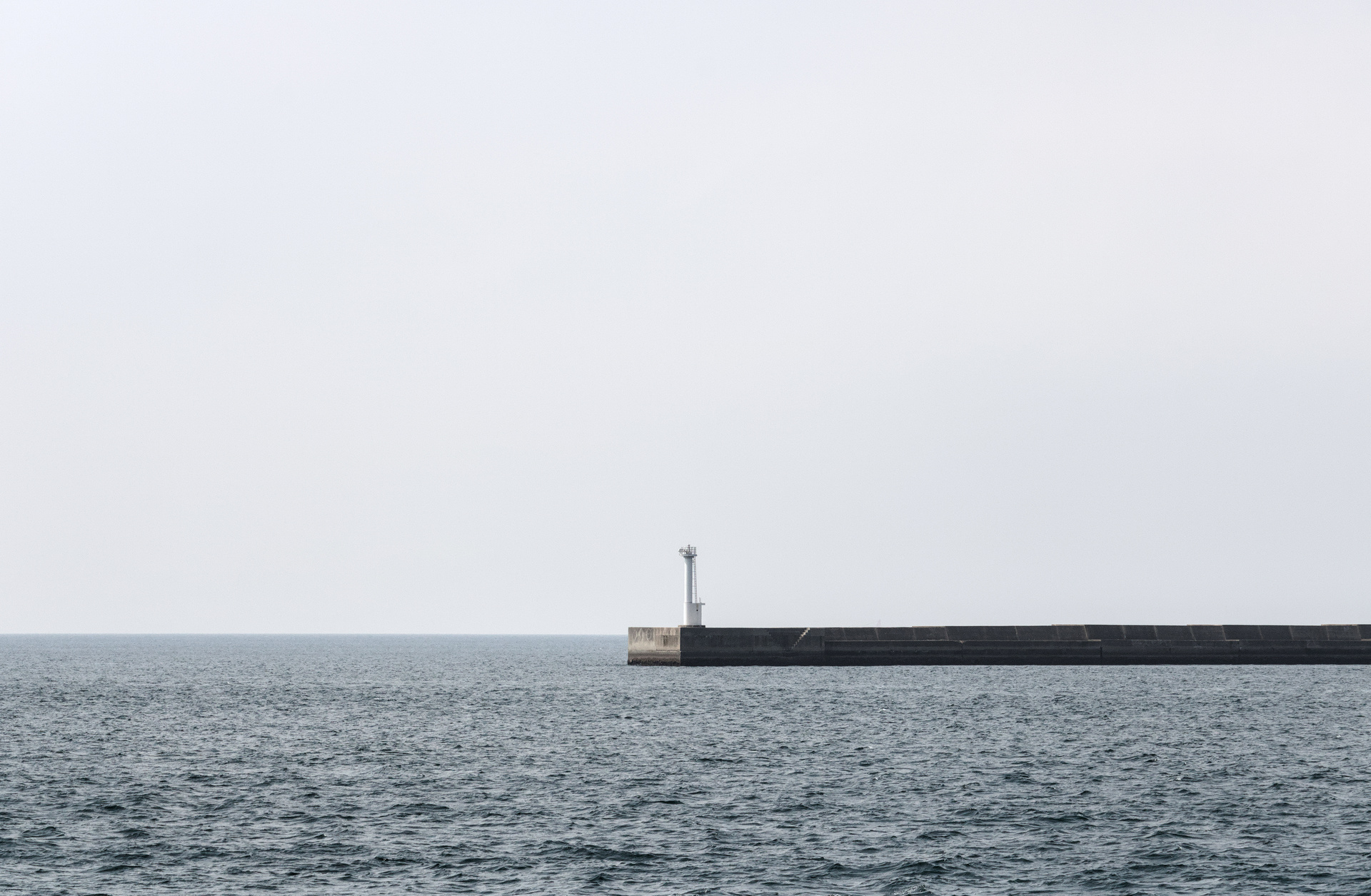 Lone lighthouse at the edge of a pier, surrounded by water and sky.
